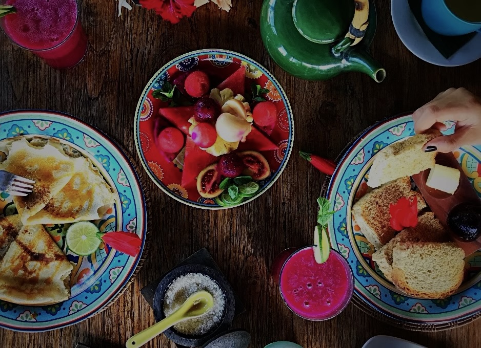 Overhead view of a breakfast spread at the Bali retreat, with pancakes, fresh fruit, bread and a pink tropical juice on a wooden table