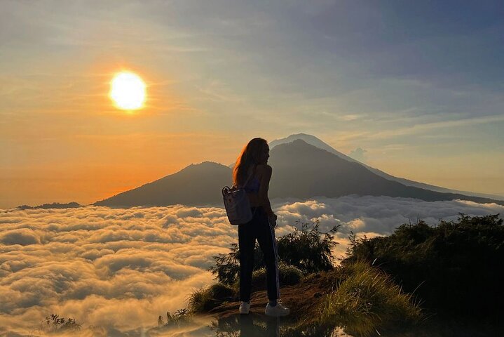 A retreat guest watching the sunrise above the clouds with a Balinese volcano in view during a mountain trek