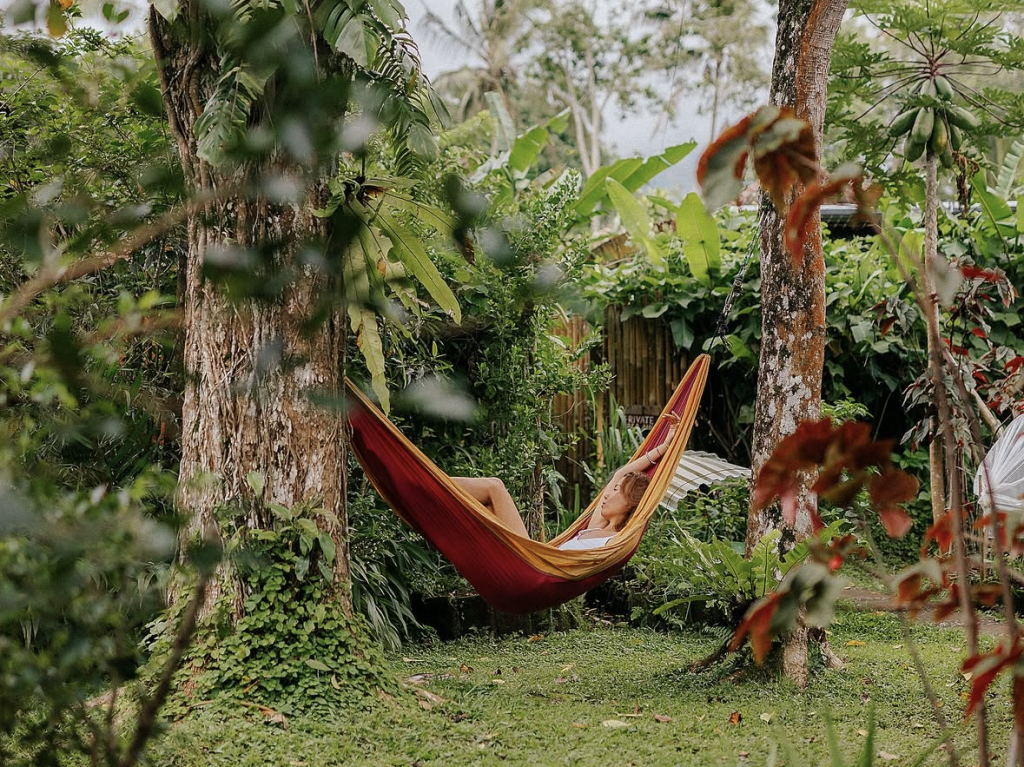 A guest relaxing in a hammock strung between trees in the lush garden at the Bali retreat