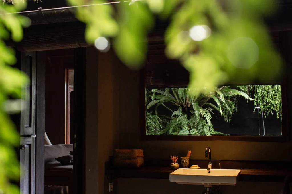 Open-air bathroom in a Bali eco-lodge bungalow, framed by tropical leaves with a mirror reflecting the surrounding jungle