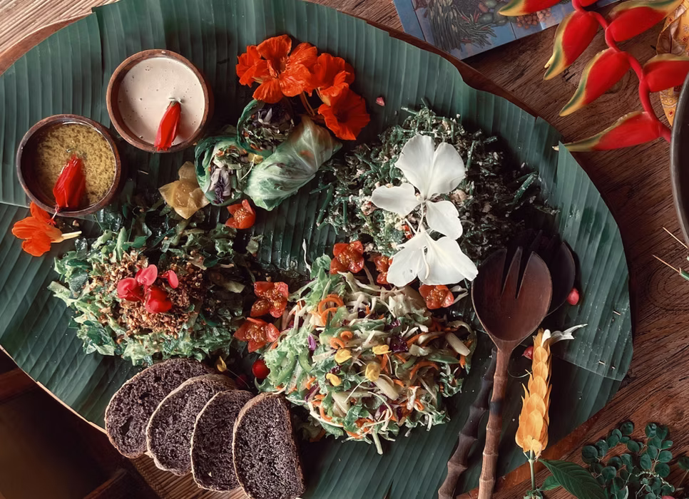 An overhead view of a colourful salad with edible flowers and dark bread on a banana leaf, part of the plant-based menu at the Bali retreat