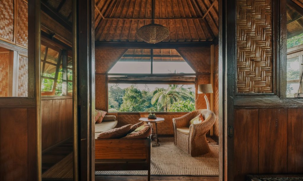 A cosy wooden lounge nook with rattan furniture at the Bali eco-lodge, opening onto a lush jungle view