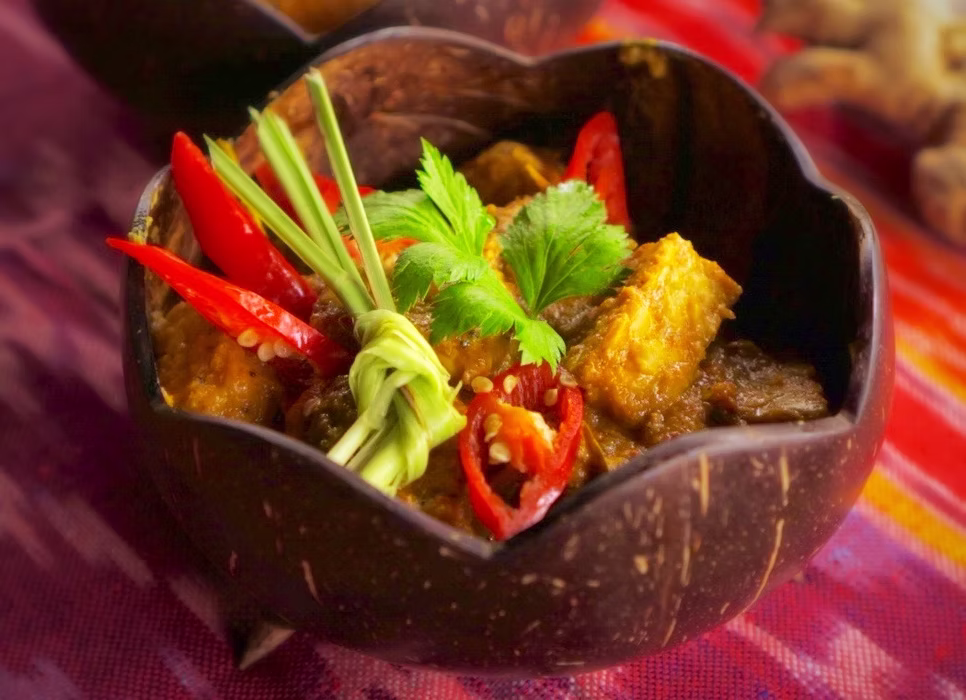 A traditional Indonesian curry dish served in a coconut shell bowl, garnished with fresh chilli and herbs, part of the local cuisine at the Bali retreat
