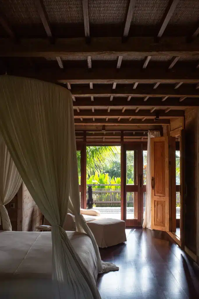 Second-floor bedroom at the Rumah Senja lodge in Bali, with a mosquito-net canopy bed opening onto a balcony overlooking the garden