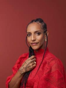 Portrait of retreat host Afua Hirsch, wearing a red lace outfit with henna-decorated hands