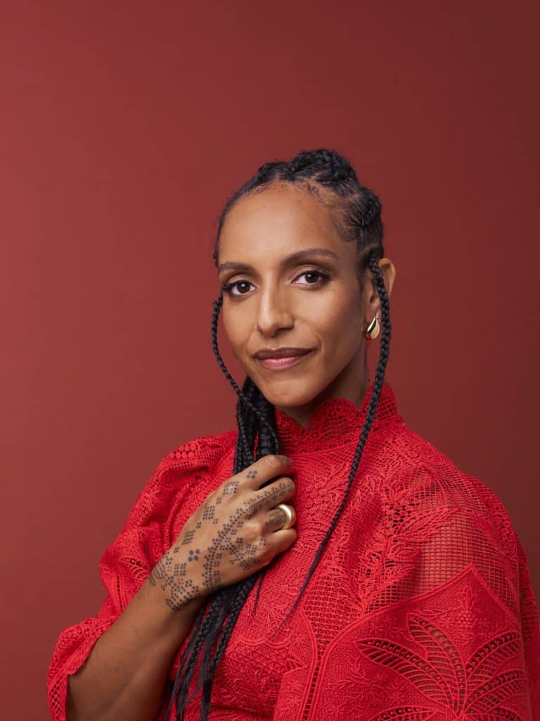 Portrait of retreat host Afua Hirsch, wearing a red lace outfit with henna-decorated hands